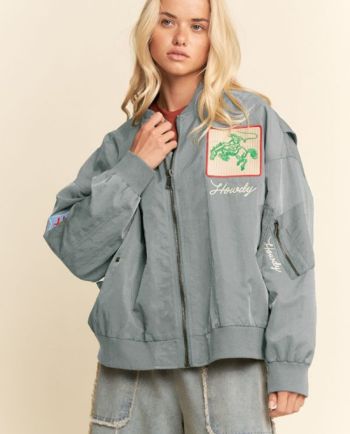 Woman modeling an oversized gray bomber jacket with “Howdy” embroidery and western-inspired patches.
