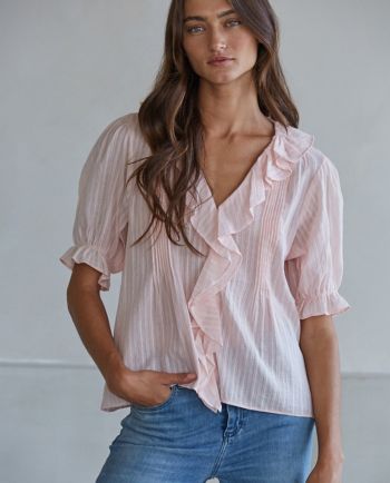 Woman wearing a light pink ruffle blouse with puff sleeves and blue jeans.