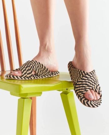 Black and tan braided rope slide sandals worn while sitting on a bright green chair.