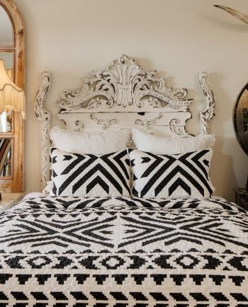 Bed with black-and-white geometric quilt and pillows, set against an ornate vintage-style headboard.