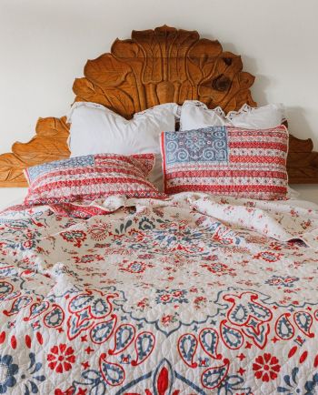 Bed with carved wooden headboard and red and blue patterned quilt and pillows.