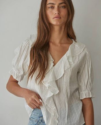 Woman wearing a light pink ruffle blouse with puff sleeves and blue jeans.