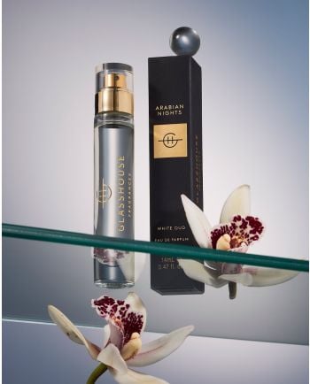 Glasshouse Fragrances Arabian Nights eau de parfum with black box displayed on glass shelf beside white orchids.