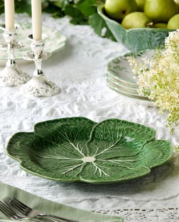 Glossy green cabbage leaf serving platter on a white lace table setting with candles and floral accents.