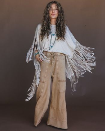 Woman modeling a light turquoise poncho top with long fringe, paired with blue flared jeans and layered jewelry.