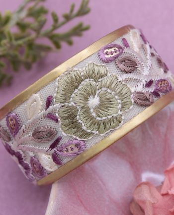 Gold-tone cuff bracelet with embroidered sage and lavender floral design on mesh fabric.