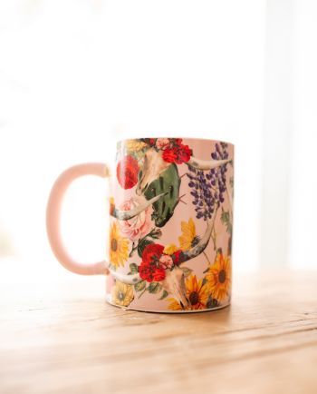 Pink ceramic mug featuring a floral longhorn skull design with colorful wildflowers and a pink handle.