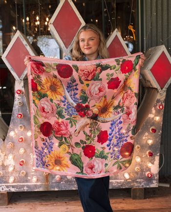Woman holding pink floral scarf with longhorn skull design in front of a lit vintage sign.