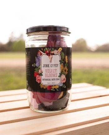 Jar of Junk Gypsy “Velvet Blooms” botanical bath soak with dried flowers and crystals, sitting on a wooden table outdoors.