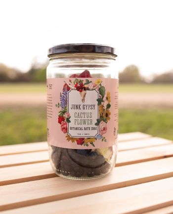 Jar of Junk Gypsy “Cactus Flower” botanical bath soak with dried botanicals, sitting on a wooden table outdoors.
