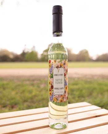 Bottle of Junk Gypsy “Cactus Flower” bubble bath with floral label, sitting on a wooden table outdoors.