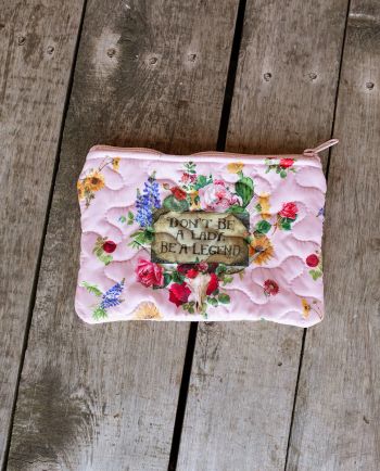 Quilted pink floral zipper pouch with a western-inspired “Don’t Be a Lady, Be a Legend” graphic on the front.