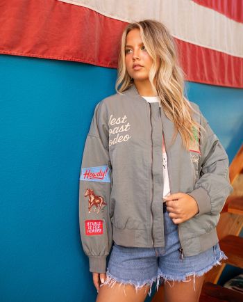 Woman modeling an oversized gray bomber jacket with “Howdy” embroidery and western-inspired patches.