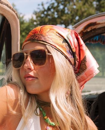 Woman wearing oversized sunglasses and a floral headscarf while sitting in a vintage truck on a sunny day.