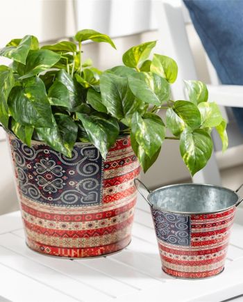 Two patterned metal buckets with red and blue boho designs, one holding a green pothos plant on a white table.